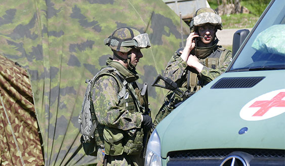 Two soldiers standing next to a green car that has a red cross on it