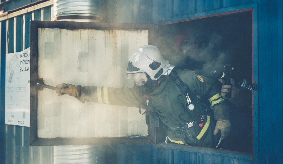 Kuvituskuva, jossa sammutuspukuun pukeutunut Suojelukomppanian varusmies avaa savua täynnä olevan kontin ikkunan osana savusukellusharjoitusta.