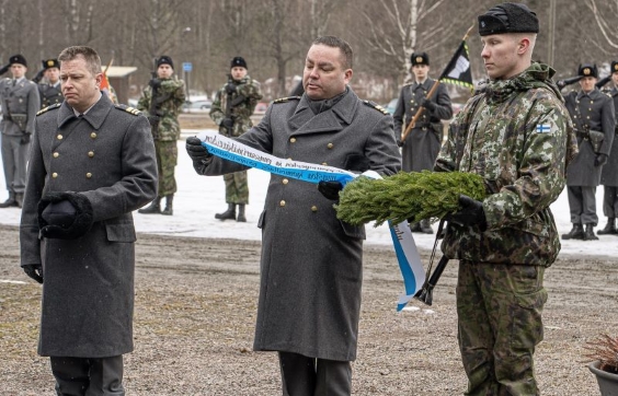 väistyvä koulunjohtaja lukee tekstiä seppeleestä, hänen vieressään seisoo uusi koulunjohtaja