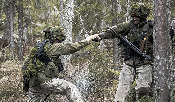 Sotilas auttaa toista sotilasta vetämällä häntä kädestä metsässä