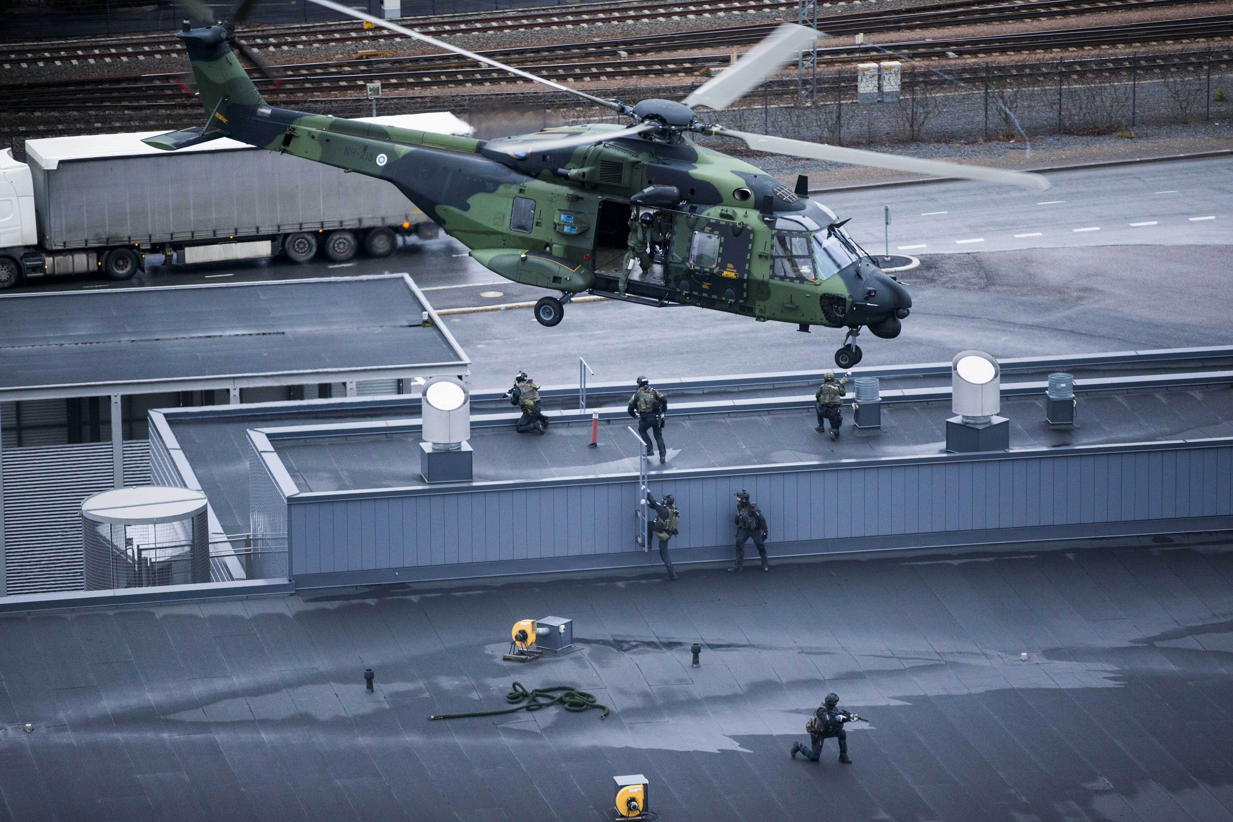 Helicopter flying over the roof that has soldiers on it.