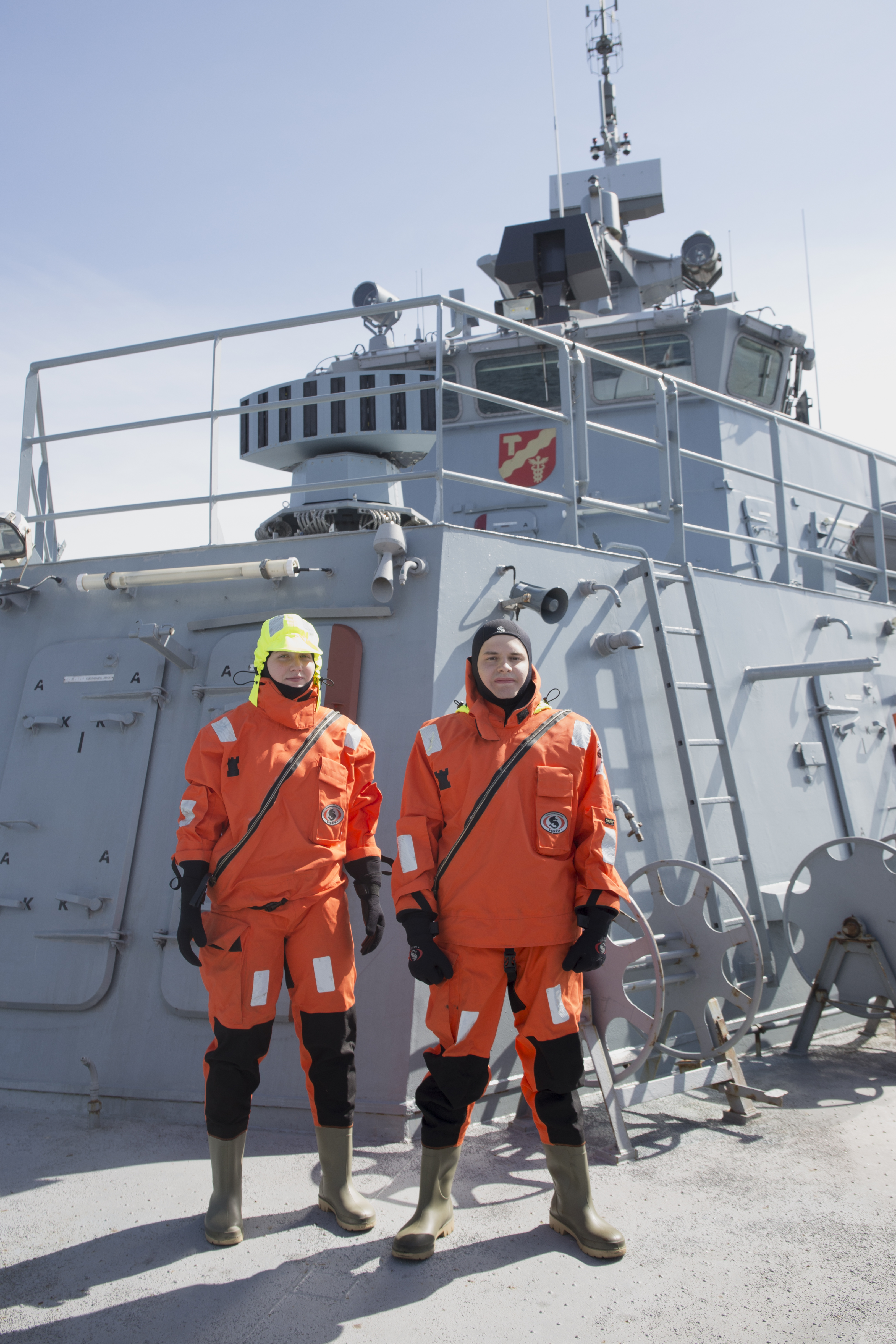 Kaksi henkilöä laivan kannella oransseissa suojapuvuissa