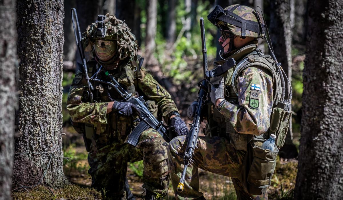 Kaksi sotilasta korkeassa polviasennossa puiden välissä