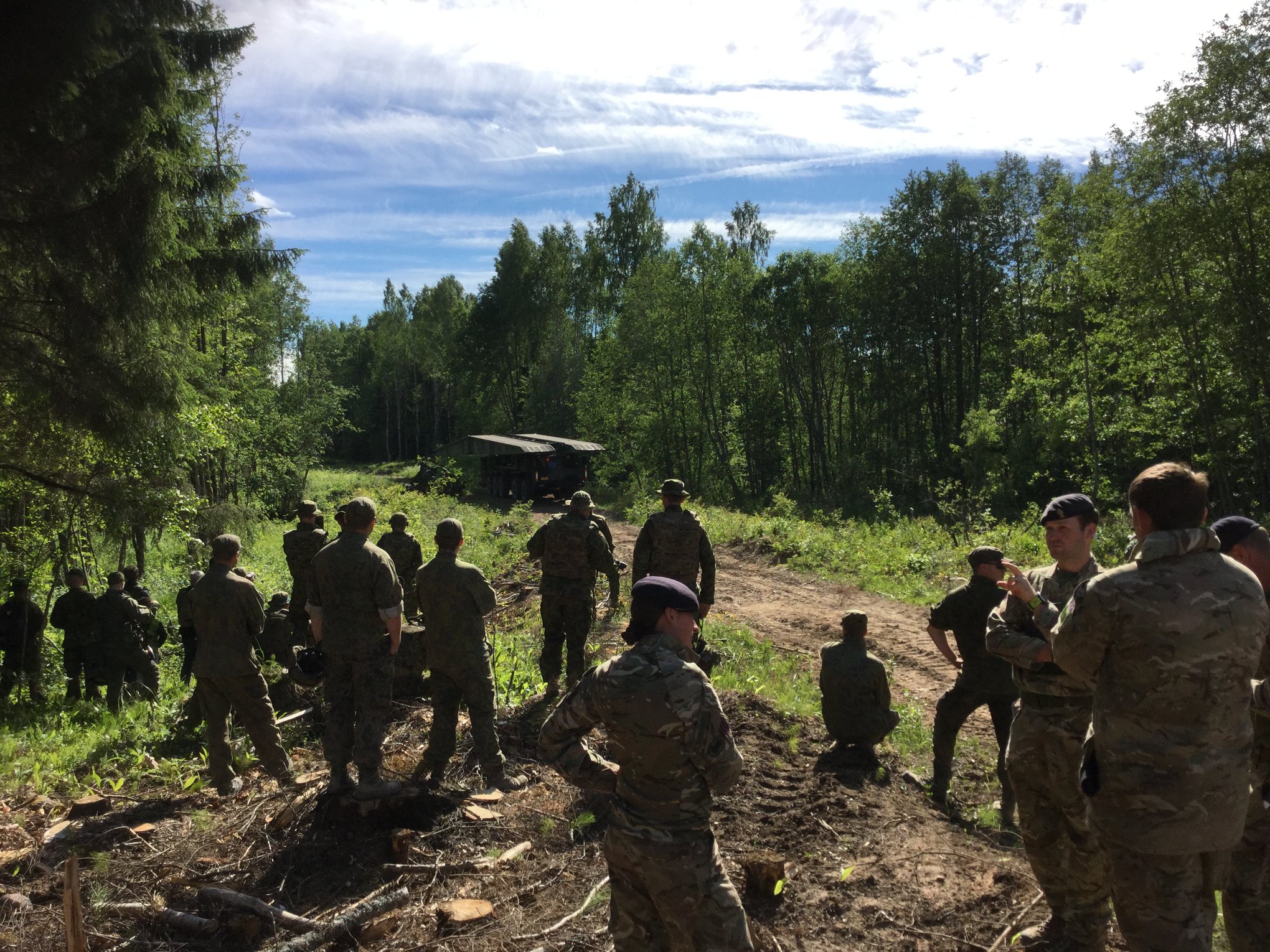 Soldiers next to a narrow forest road. A bridge vehicle in the background.