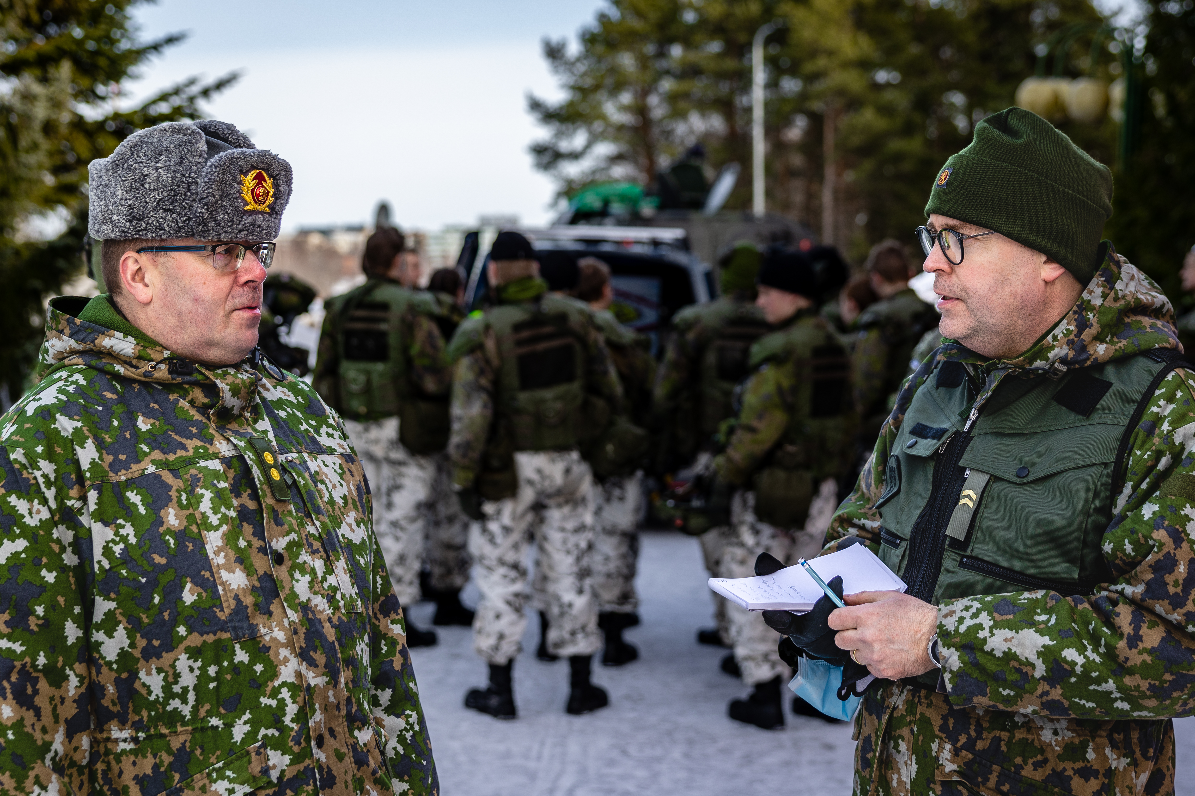 Everstiluuntantti Pasi Heinua vasemmalla haastateltavana, taustalla sotilaspoliisijoukko.