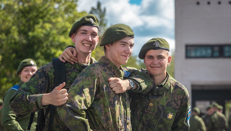 Kolme maastopukuista sotilasta katsoo hymyilee ja katsooo kameraan kasarmialueella