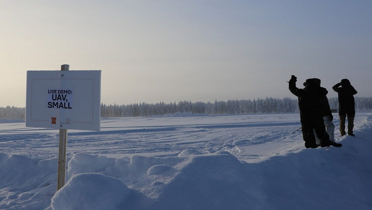 Kolme toppa-asuun pukeutunutta henkilöä seuraa UAV-esittelyä lumisessa maastossa