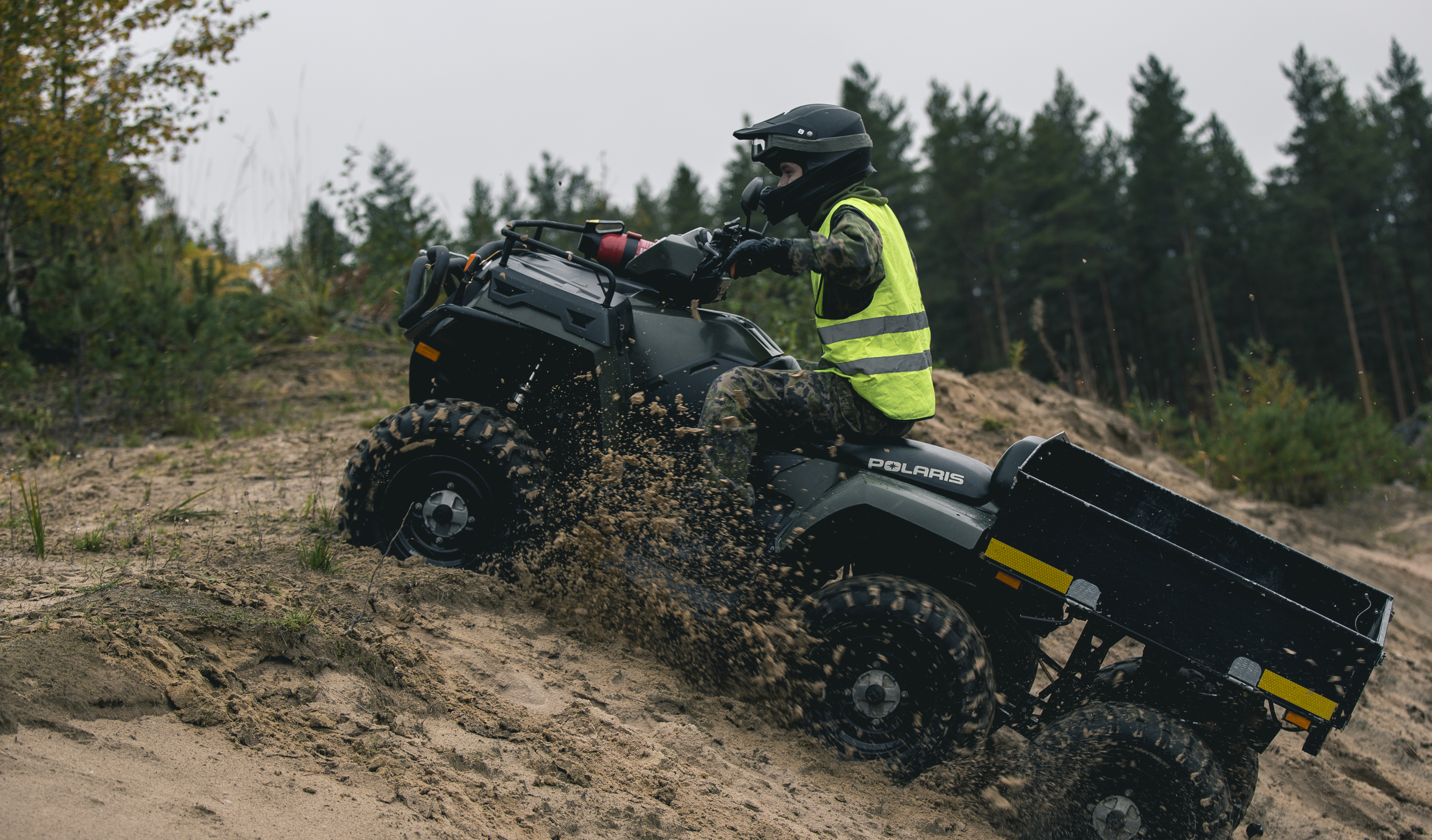 A soldier rides a quad bike on a sandy uphill with a safety vest on