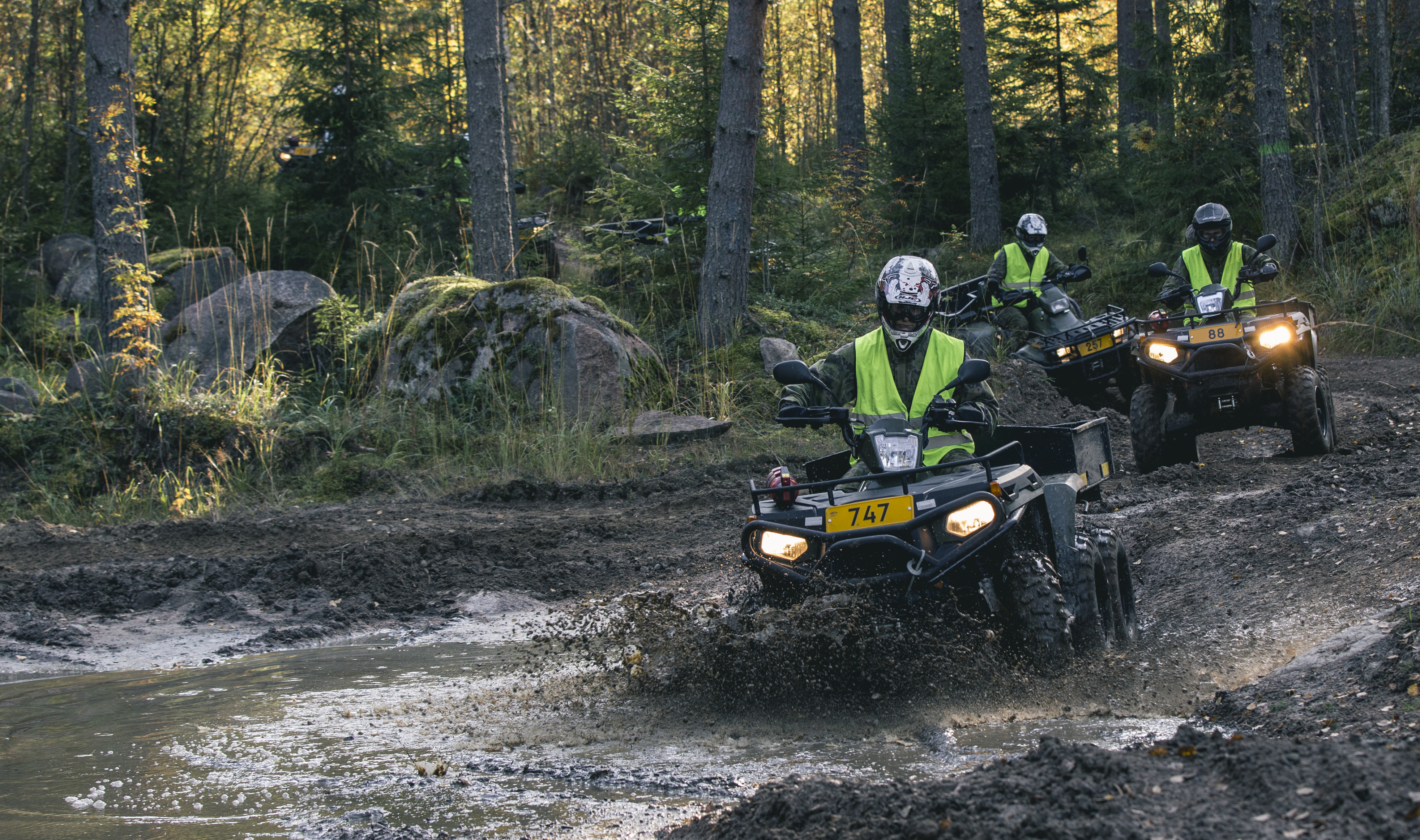 Soldiers ride over a puddle of water on quad bikes